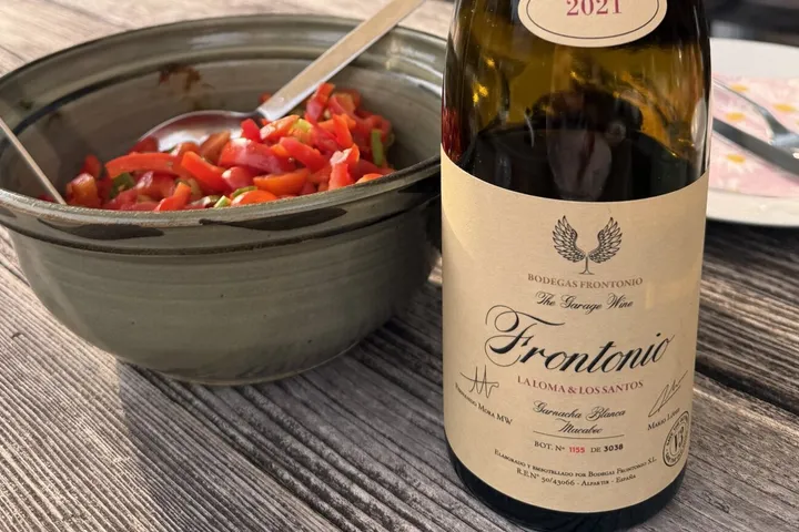 Flasche Frontonio La Loma & Los Santos 2021 mit lesbarem Etikett auf einem verwitterten Holztisch, daneben eine Schale mit Paprikasalat