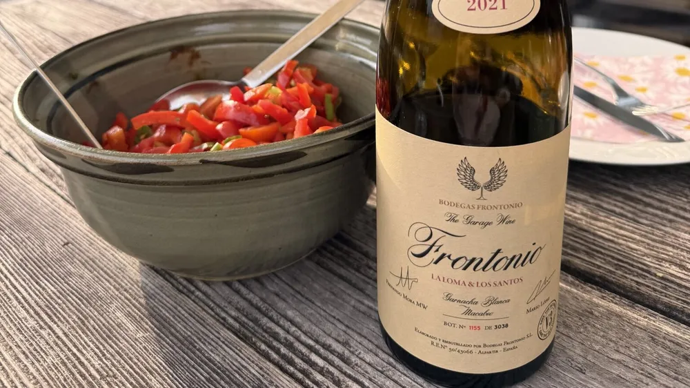 Flasche Frontonio La Loma & Los Santos 2021 mit lesbarem Etikett auf einem verwitterten Holztisch, daneben eine Schale mit Paprikasalat