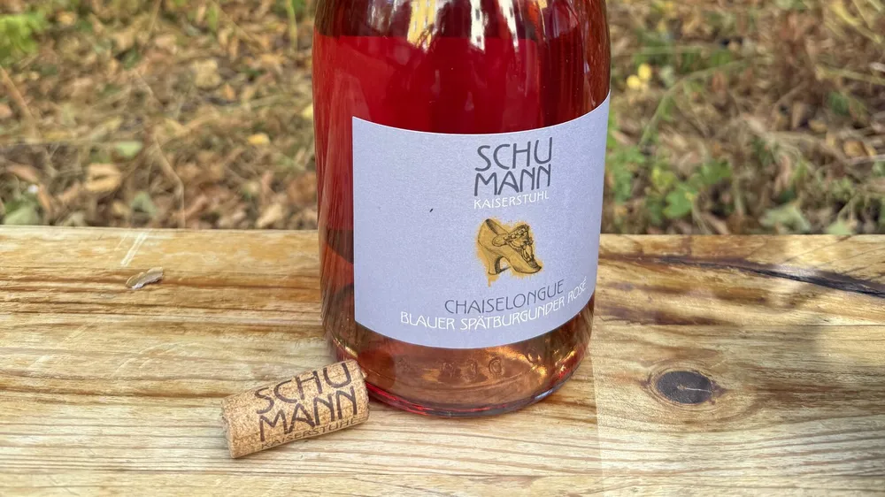 Geöffnete Magnumflasche Schumann Chaiselongue Blauer Spätburgunder Rosé 2022 mit gebrandetem Korken auf einer Holzbank im Garten