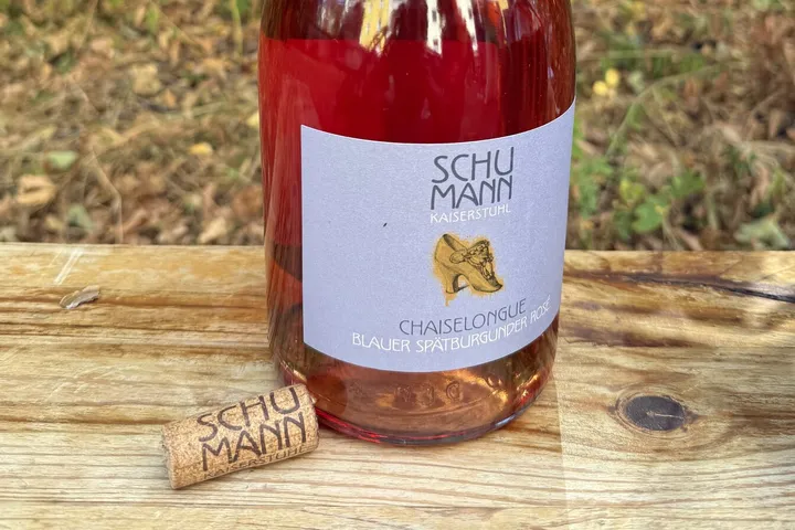 Geöffnete Magnumflasche Schumann Chaiselongue Blauer Spätburgunder Rosé 2022 mit gebrandetem Korken auf einer Holzbank im Garten