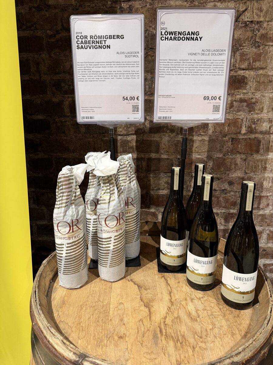 Flaschen von LÖWENGANG Chardonnay 2021 und COR RÖMIGBERG 2018 auf einem Fass im Kölner Weinkeller