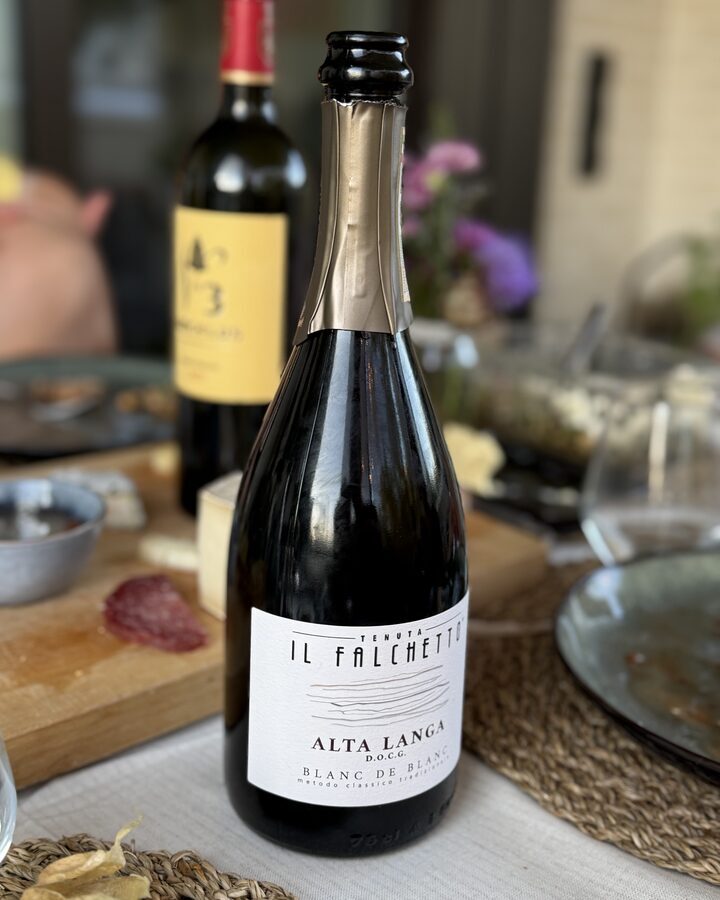 Flasche Tenuta Il Falchetto Alta Langa Blanc de Blancs auf dem Balkontisch, dahinter unscharf die Flasche No 3 d'Angelus
