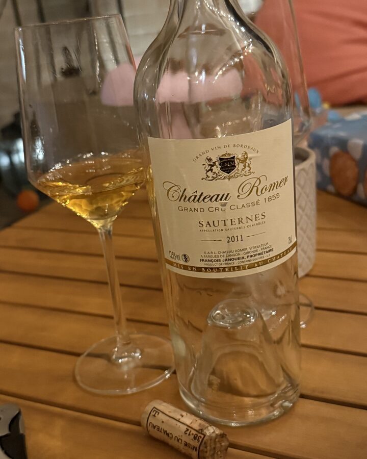 Fast leere Flasche Château Romer Sauternes 2011 mit gefülltem Glas und Korken auf einem Holztisch am Abend