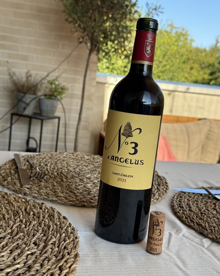 Flasche No 3 d'Angelus Saint-Émilion 2021 mit gebrandetem Korken auf dem gedeckten Balkontisch im Abendlicht