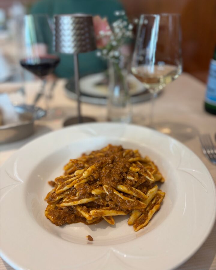 Casarecce mit Kalbsragout im tiefen weißen Teller, im Hintergrund ein Weißwein- und ein Rotweinglas
