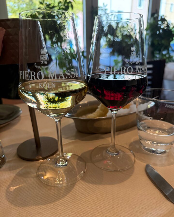 Ein Glas Weißwein und ein Glas Rotwein mit Gravur auf heller Tischdecke vor der Fensterfront des Restaurants