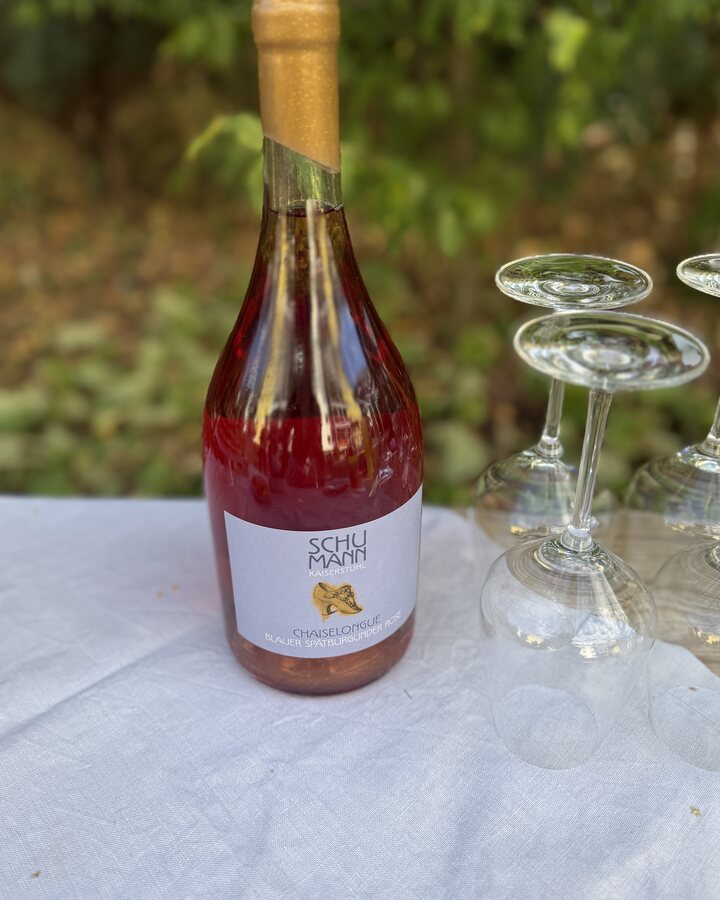Ungeöffnete Magnumflasche Chaiselongue Rosé mit Wachskapsel neben gestürzten Weingläsern auf weißer Tischdecke