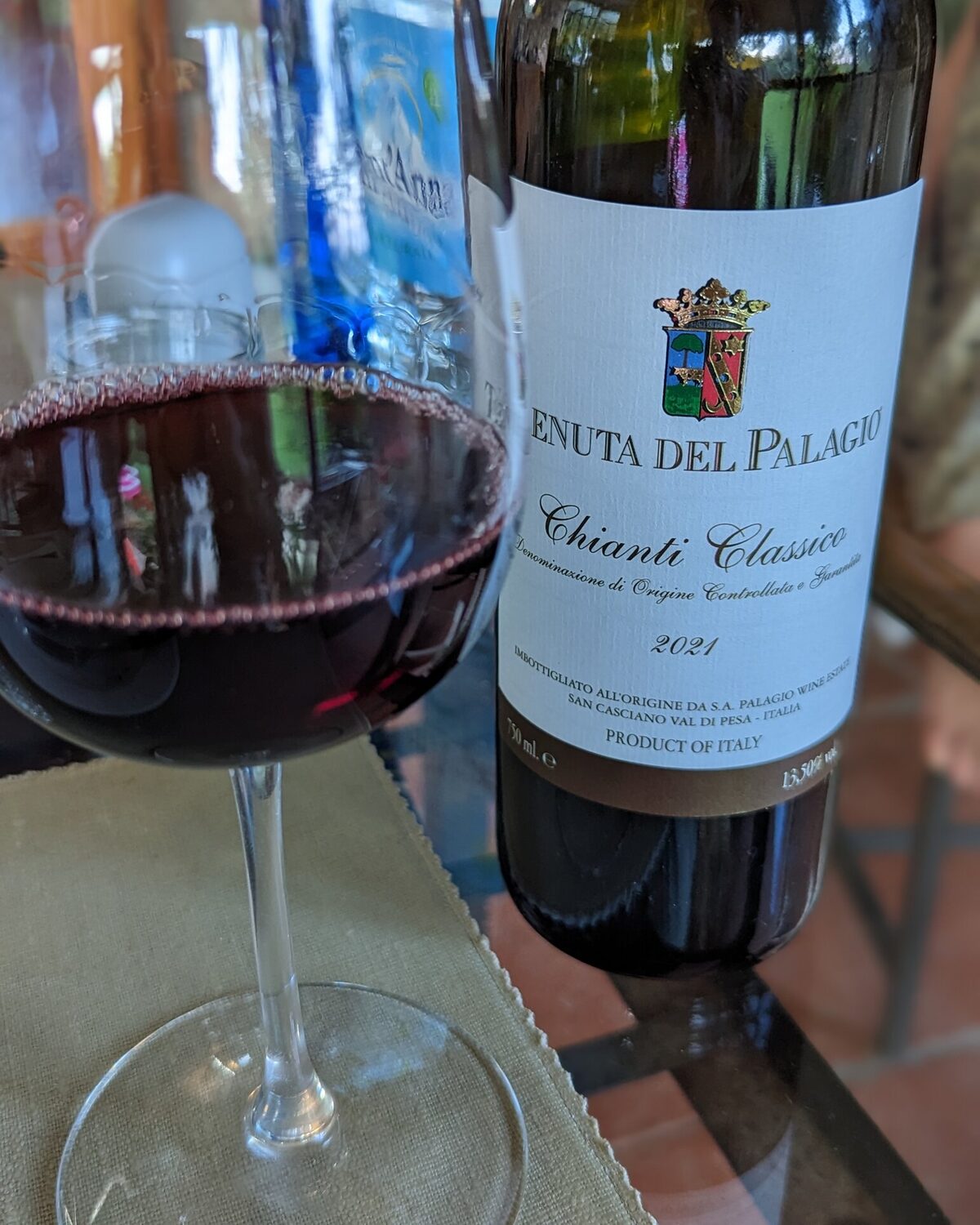 Flasche Chianti Classico der Tenuta del Palagio, Jahrgang 2021, neben einem gefüllten Rotweinglas auf einem Tisch